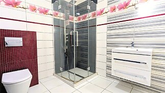 Moderní koupelna s dlažbou, sprchovým koutem a vzorovanými obklady. Světlá keramika a praktické umyvadlo dotvářejí elegantní design.