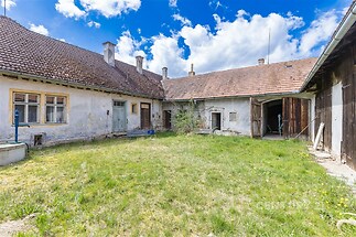 Uzavřený dvůr s rustikálním stavením, původní omítka, dřevěná vrata a tráva. Ideální pro renovaci a přetvoření na venkovskou oázu.