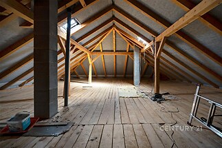 Podkrovní prostor se dřevěnými trámy, dřevěnou podlahou a střešním oknem, ideální pro vestavbu dalších místností či úložných prostor v domě.