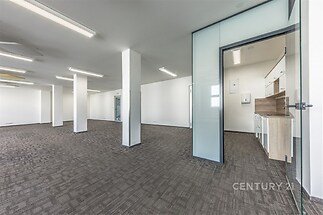 Prostorná kancelář s moderními skleněnými příčkami, kobercovou podlahou a vestavěnou kuchyňkou, vhodná pro komerční využití.