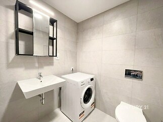 Moderní koupelna s dlažbou, která zahrnuje zrcadlovou skříňku a pračku, nabízí praktické a čisté řešení s moderním designem.