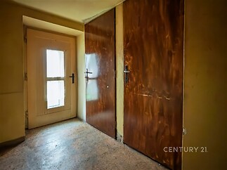 Chodba s dřevěnými dveřmi, linoleem na podlaze a velkým oknem přinášejícím přirozené světlo.