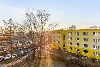 Žlutý panelový dům s velkými okny, okolní zeleň, klidná lokalita, blízkost městské infrastruktury, slunečný výhled.