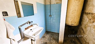 Malá koupelna s modrými dlaždicemi, umyvadlem a betonovou podlahou. Prostor vyžaduje rekonstrukci, ale nabízí potenciál pro modernizaci.