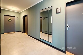 Chodba s moderní dlažbou, velkým zrcadlem a tmavými dveřmi nabízí elegantní a prostorný vstup do bytu.