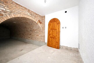 Vinný sklep s cihlovou klenbou, dřevěnými dveřmi a betonovou podlahou, ideální pro skladování vína nebo přestavbu na společenskou místnost.