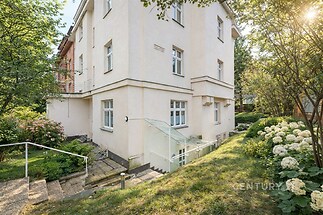 Venkovní pohled na dům s udržovanou zahradou, světlá fasáda, moderní vstupní schodiště, klidná lokalita.