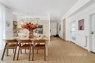 Prostorná kuchyň s moderním designem, dlažbou a vestavěnými spotřebiči, světlá jídelna s dřevěným nábytkem a velkými okny poskytuje pohodlí.