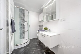 Moderní koupelna s dlažbou, sprchovým koutem a vestavěnými skříněmi, světlý prostor s bílým obkladem a elegantním designem