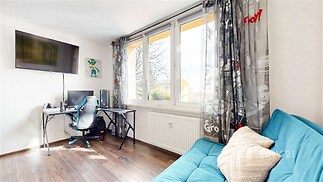 Světlý studentský pokoj s parketovou podlahou a velkými okny, moderní pracovní stůl, pohodlná pohovka, ideální prostor pro studium a relaxaci.