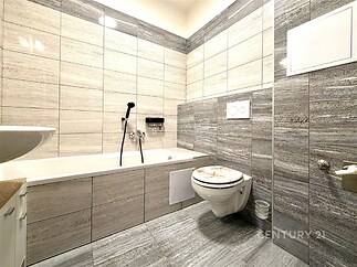 Moderní koupelna s šedými obklady, závěsnou toaletou a vanou. Světlý prostor s kvalitní dlažbou a čistým designem.