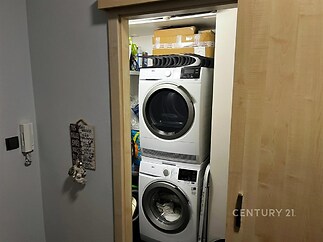 Malá prádelna s moderní pračkou a sušičkou, posuvné dveře, vestavěné úložné police, dřevěný rám dveří.