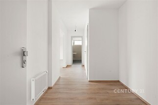 Světlá chodba s parketovou podlahou, bílými stěnami a novými dveřmi, vedoucí do moderní koupelny s velkým oknem.