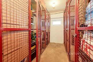 Venkovní sklepní prostor s kovovou mříží, betonovou podlahou a malým oknem. Sklep je suchý a vhodný pro uskladnění nebo jako úložný prostor.