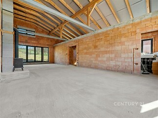 Prostorný obývací pokoj s betonovou podlahou, velkými okny a odhalenými dřevěnými trámy, v moderním stavu ideální pro vlastní úpravu.