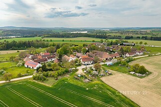 Pohled na malebnou vesnici obklopenou zelenými poli a loukami, s tradičními domy a klidným venkovským prostředím.
