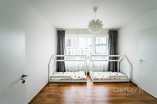 Dětský pokoj s parketovou podlahou, velkými okny a bílými stěnami. Světlý a moderní design, ideální pro rodiny s dětmi.