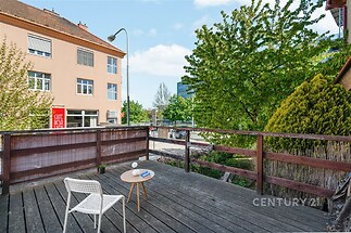 Prostorná terasa s dřevěnou podlahou nabízí výhled na klidné městské prostředí, ideální pro odpočinek a volný čas, udržovaná a moderní.