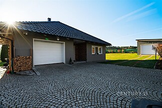 Moderní rodinný dům s dlážděným nádvořím, garážovými vraty a elegantní fasádou. Klidná lokalita, dobře udržovaná zahrada.