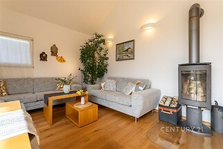 Světlý obývací pokoj s krbovými kamny, dřevěnou podlahou a moderním nábytkem nabízí útulné a stylové prostředí.