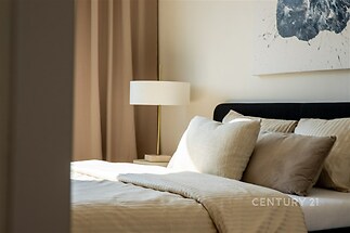 Prostorná ložnice s moderním designem, světlé ložní prádlo a tlumené osvětlení, velká okna zajišťují dostatek denního světla.