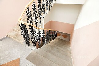 Schodiště s ozdobným kovovým zábradlím, mramorová dlažba, světlé stěny, historický styl, udržovaný stav.