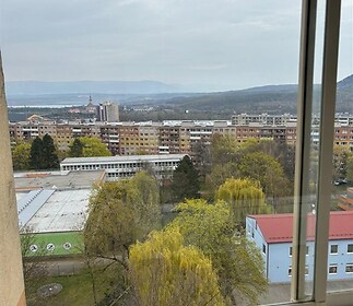Výhled z balkonu v panelovém domě s výhledem na město a zeleň, okna s plastovým rámem, klidná lokalita poblíž centra.