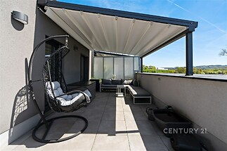 Prostorná terasa s dlažbou, moderním zastřešením a designovým nábytkem, ideální pro relaxaci, s výhledem na okolní krajinu.