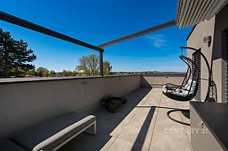 Prostorná terasa s moderní dlažbou, vybavená stylovým závěsným křeslem, ideální pro relaxaci a s krásným výhledem na okolní přírodu.