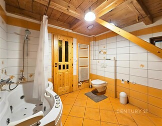 Podkrovní koupelna s dlažbou, dřevěným stropem a rohovou vířivou vanou, vybavená závěsným WC a topením.