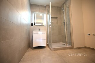 Moderní koupelna s dlažbou a sprchovým koutem. Prostorné zrcadlo se skříňkou pod umyvadlem zvýrazňuje elegantní a praktický design.