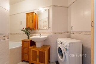 Koupelna s moderními obklady, dřevěným nábytkem a zabudovanou pračkou. Světlý prostor s elegantními liniemi a kvalitními materiály.