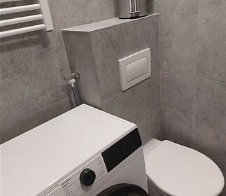 Koupelna s moderními obklady, nástěnnou toaletou a pračkou značky Gorenje, vytápění zajišťuje sušák na ručníky.