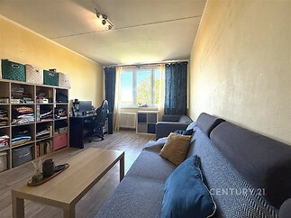 Obývací pokoj s parketovou podlahou, velkými okny a moderním nábytkem, což zajišťuje světlý a útulný prostor pro relaxaci či práci.