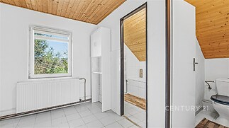 Podkrovní koupelna s dlažbou, dřevěným stropem a velkým oknem. Světlý prostor s vanou a toaletou, moderní úprava vhodná k rekonstrukci.