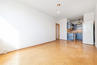 Světlý obývací pokoj s parketovou podlahou, moderní kuchyní a velkými okny, které poskytují dostatek přirozeného světla.