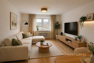 Světlý obývací pokoj s parketovou podlahou, velká okna s výhledem, moderní nábytek a minimalistická dekorace.