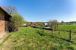 Prostorná zahrada s venkovským výhledem, trávník udržovaný, oplocení ze dřeva a drátěného pletiva, ideální pro relaxaci a zahradničení.
