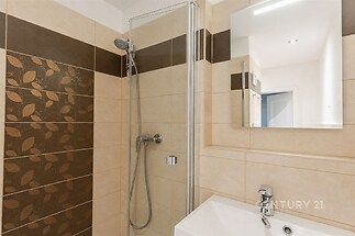 Koupelna s moderní dlažbou, sprchovým koutem a zrcadlem. Díky kombinaci béžových a hnědých kachliček působí stylově a elegantně.