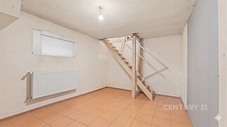 Prázdný sklepní prostor, dlažba na podlaze, dřevěné schody, bílé stěny, jednoduché osvětlení, vhodný pro úložné prostory nebo dílnu.