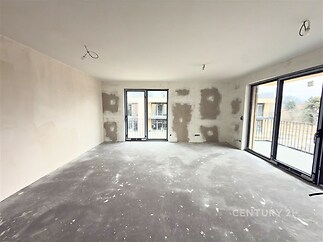 Prázdný obývací pokoj s velkými okny, betonovou podlahou a moderními prvky, připravený k dokončení nebo rekonstrukci.