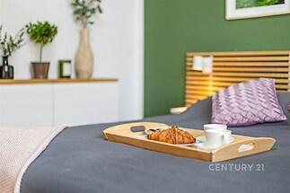 Stylová ložnice s moderní výzdobou, zelenou akcentní stěnou a dřevěným čelem postele. Světlé dekorace vytvářejí útulnou atmosféru.