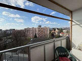 Balkon s výhledem na městskou zástavbu, kovové zábradlí, bezpečnostní síť, slunečné počasí, vhodné pro venkovní posezení