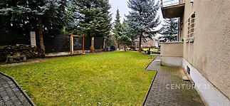 Zahrada s udržovaným trávníkem, obklopená stromodřevěným plotem a chodníkem z dlažby, nabízí klidné prostředí pro relaxaci.