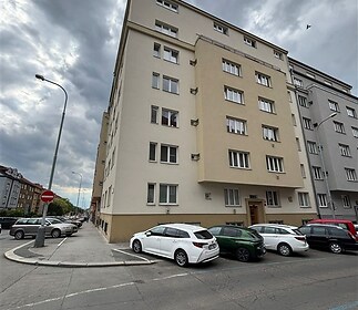 Bytový dům s rekonstruovanou fasádou, velkými okny a parkováním před budovou, situovaný v klidné městské lokalitě.