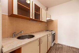 Kompaktní kuchyně s moderními spotřebiči, dlažbou na stěnách a dřevěnou podlahou, nabízí praktické využití prostoru a světlý design.