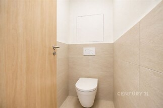 Samostatná toaleta s moderními dlaždicemi a dřevěnými dveřmi, světlý design vytváří elegantní a čistý prostor.