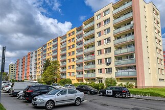 Řadový panelový bytový dům s barevnými fasádami, určený k prodeji nebo pronájmu. Parkovací místa před domem, moderní komunitní bydlení.