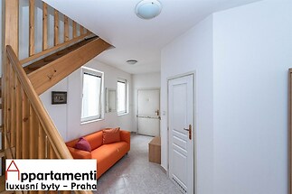 Vstupní hala s dlažbou, dřevěné schodiště s moderním designem, světlý prostor s velkými okny, pohodlná sedací souprava.