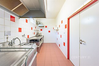 Kuchyň s dlažbou a bílými obklady, sporákem a odsavačem par, vhodná pro komerční využití nebo gastro provoz.